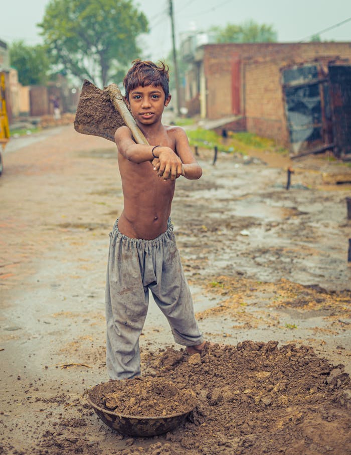 A child holding a shovel in a rural setting, conveying innocence and hard work.