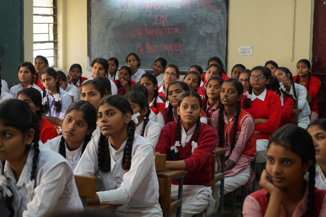 Group of Indian schoolgirls in uniform attentively listening in a classroom setting.